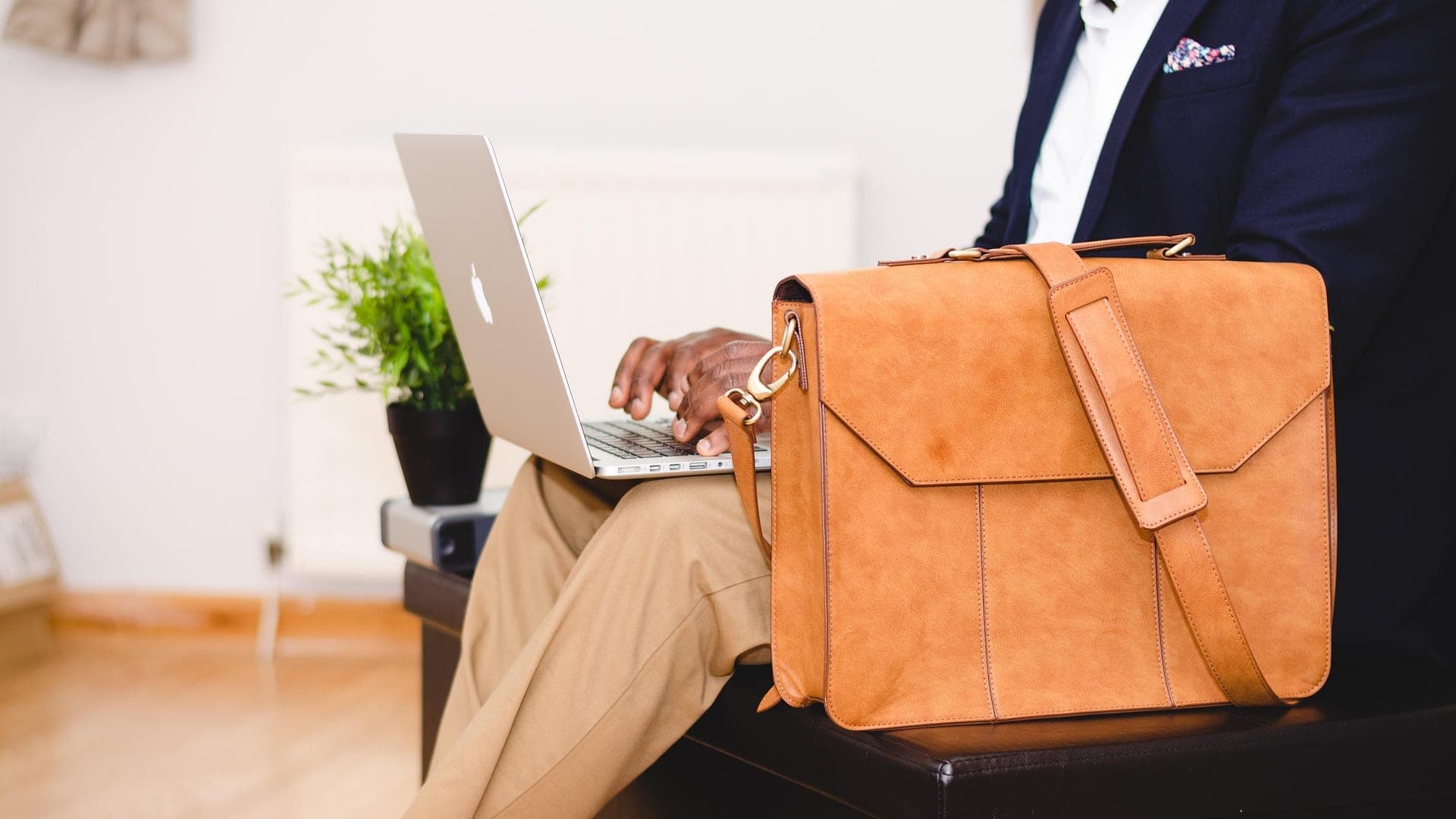 Homem de terno com notebook no colo e uma pasta de couro ao lado