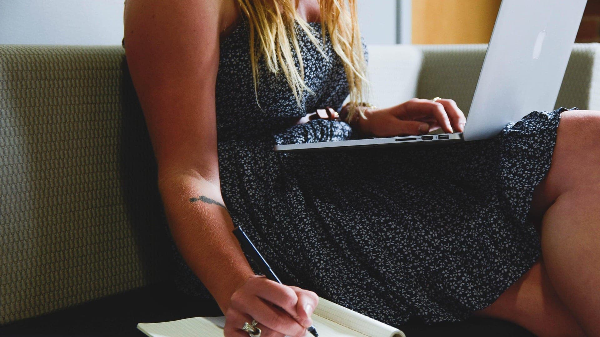 Mulher com notebook no colo fazendo anotações num caderno