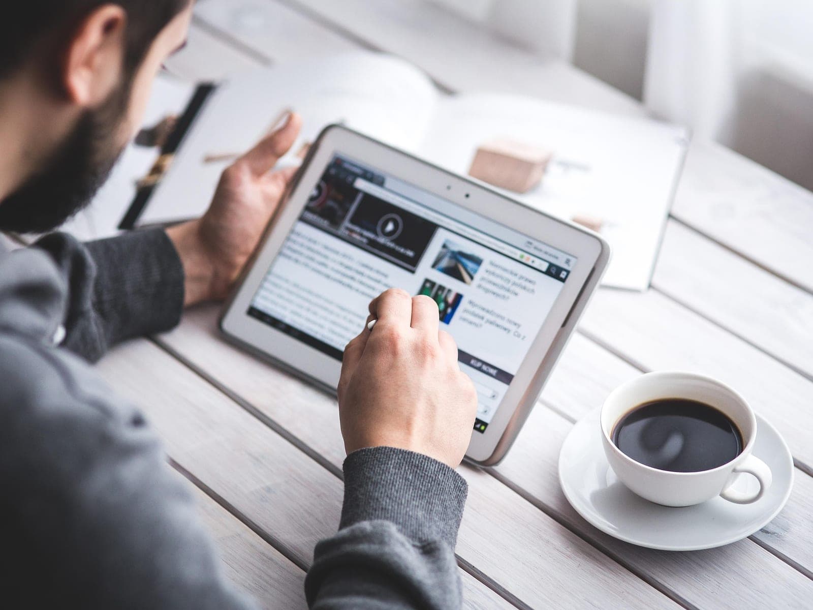 Homem usando um tablet numa mesa de madeira, ao lado de uma xícara de café