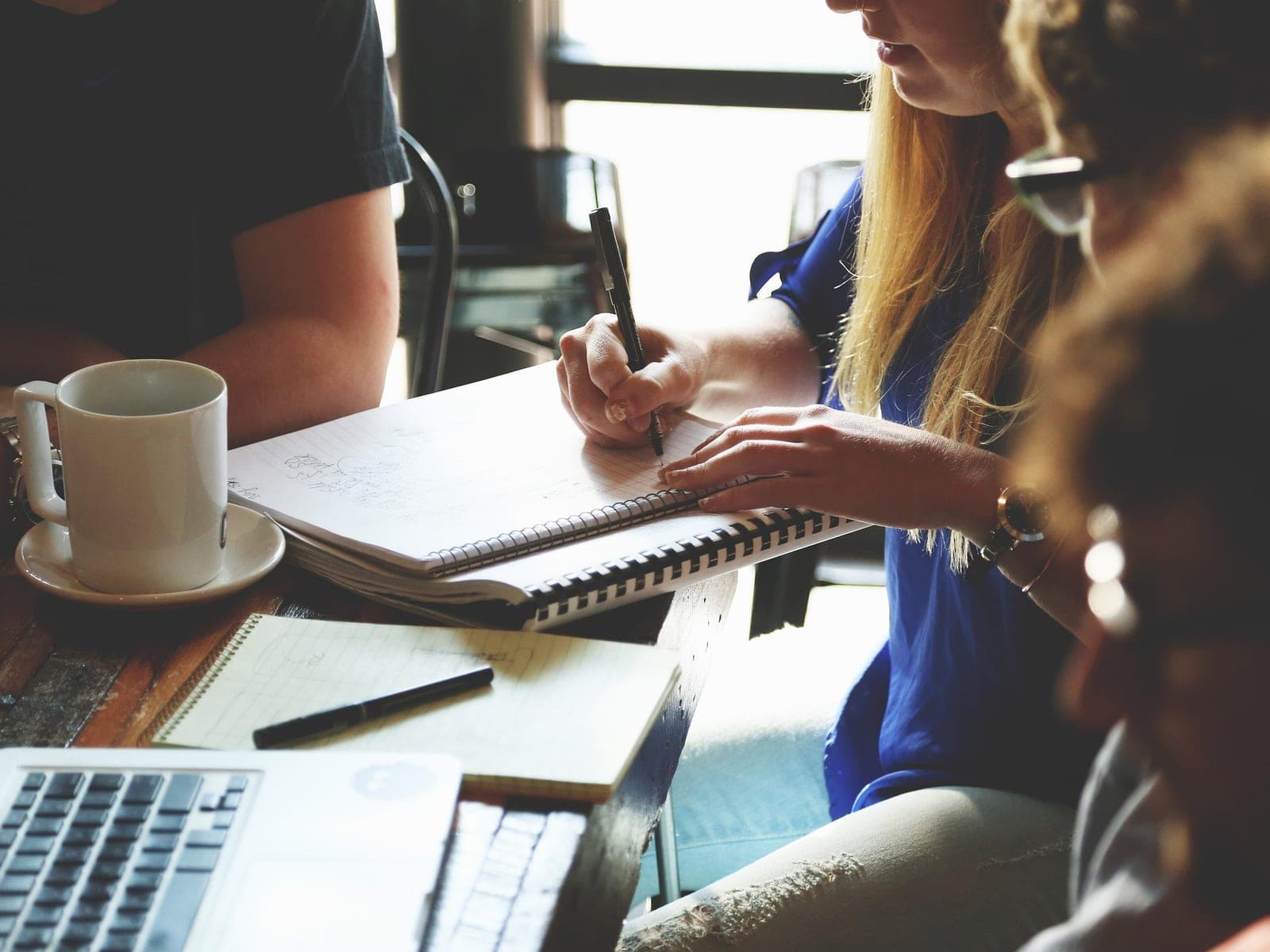 Equipe reunida numa mesa com cadernos, notebook e café