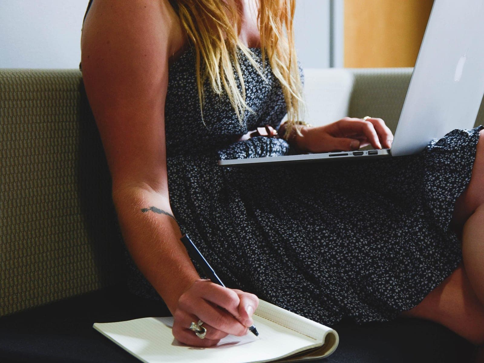 Mulher com notebook no colo fazendo anotações num caderno